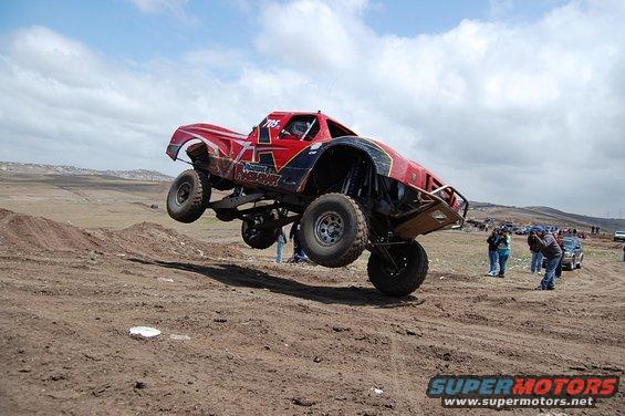 Red off-road truck airborne over dirt track