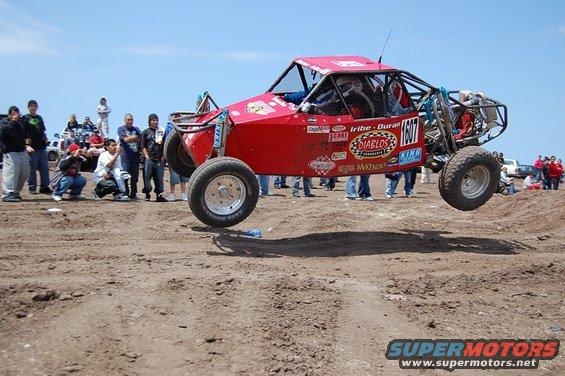 red off-road buggy mid-air jump, number 1607 on door, crowd watching