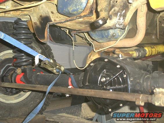 close-up of vehicle's rear axle and suspension components, with a blue strap securing the spring