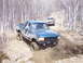 1996 Ford Bronco - Two off-road vehicles navigate a muddy trail through a forest with bare trees.