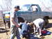 1996 Ford Bronco - Three men are gathered around the underside of a muddy green Ford Bronco, appearing to perform repairs.