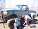 1996 Ford Bronco - Three individuals are gathered around a muddy green Ford Bronco, appearing to perform repairs or modifications on its lifted suspension.
