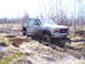 1996 Ford Bronco - A GMC pickup truck is deeply stuck in thick mud and water, surrounded by sparse vegetation and trees.