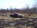 1996 Ford Bronco - A red pickup truck navigates a muddy, wooded terrain, its grille indicating an early 2000s model year.