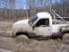 1996 Ford Bronco - A white pickup truck is deeply stuck in mud, with a person visible in the driver's seat.