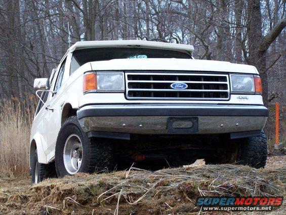 White Ford Bronco parked on a dirt incline with trees in the background