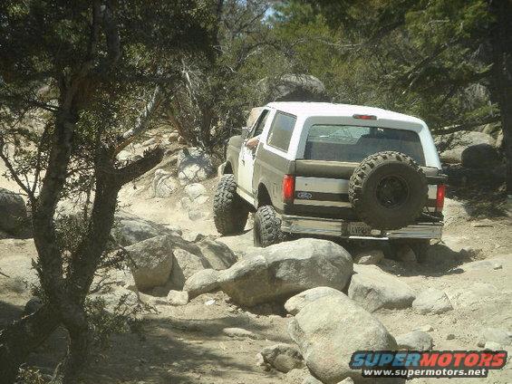 Two-tone brown and white Ford Bronco off-roading over rocks
