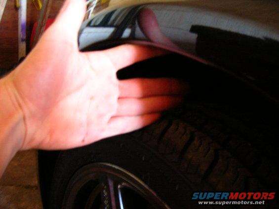 Hand reaching into black car wheel well near tire and rim