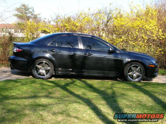 Black sedan parked on grass, side view. Tinted windows, aftermarket wheels, spoiler