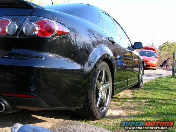 Black sedan, rear quarter panel and side view. Red car in background