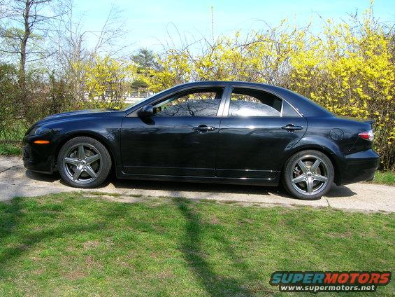 Black sedan parked on a gravel driveway with green grass and yellow flowering bushes
