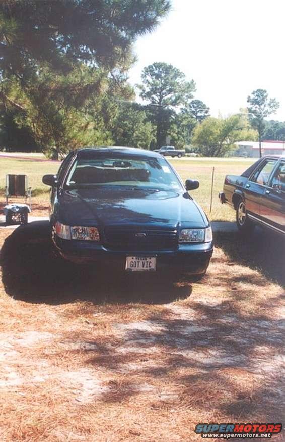 Dark blue Ford Crown Victoria parked outside, license plate says 'GOT VIC'. Another car is parked to the right