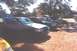 2002 Ford Crown Victoria - A line of sedans, including a dark 2002 Ford Crown Victoria with its hood and driver door ajar, are parked outdoors.
