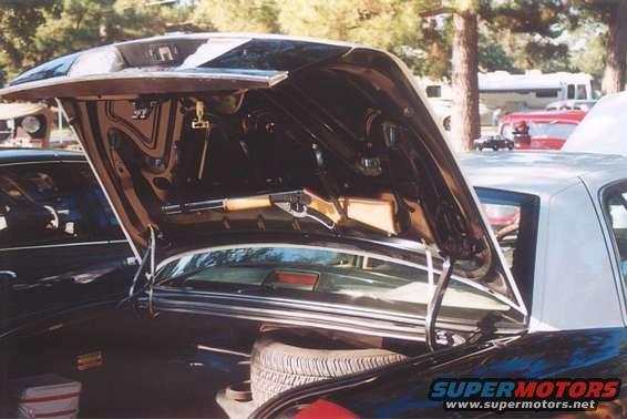 Car trunk open, showing spare tire and some storage. Another car is visible to the left. RVs and a red car are in the background