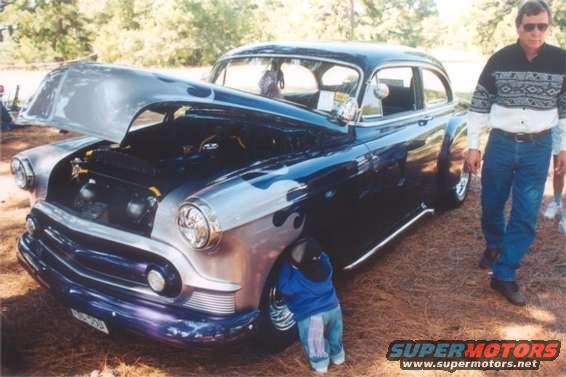 Customized classic sedan with hood open, flames on the side, and a child peeking from behind the front wheel