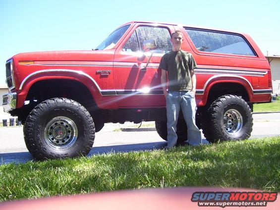 1986 Ford Bronco lifted with large tires, person standing beside it