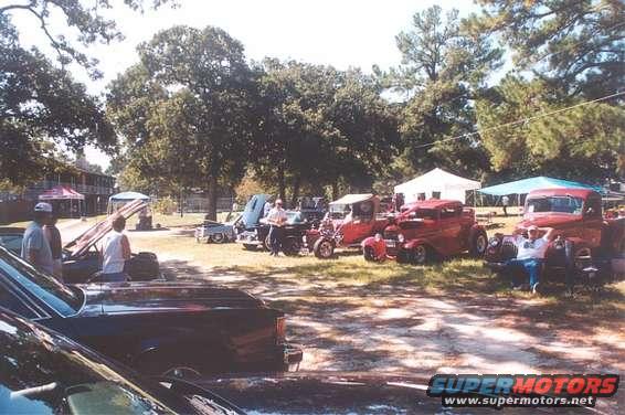 Several vintage red cars and trucks parked outdoors with people around them