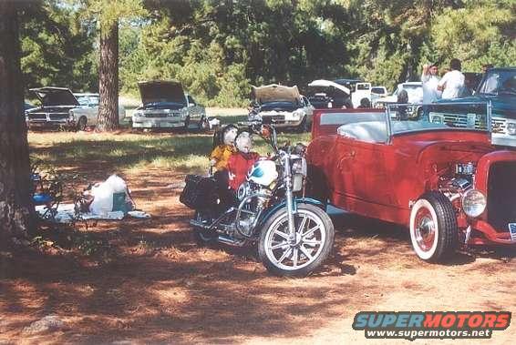 Motorcycle with two figures parked next to a red hot rod
