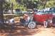 2002 Ford Crown Victoria - A motorcycle with two figures is parked next to a red hot rod at an outdoor gathering with several other vehicles.