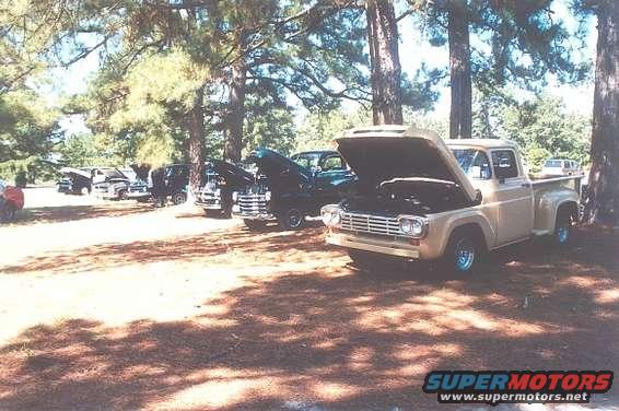 Tan pickup truck with hood open, parked on dirt under trees