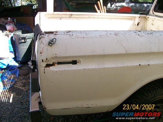 White pickup truck bed with rust and peeling paint, viewed from the rear quarter. A black trash can is to the left