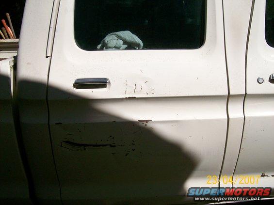 Side view of a white pickup truck's doors. Some damage and scratches are visible on the lower door panel