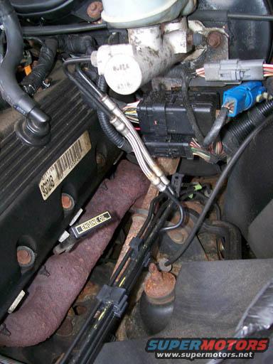 Engine bay showing brake fluid reservoir, wiring harnesses, and exhaust manifold. Label reads 'ENGINE OIL'