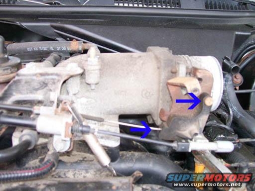 Close-up of a vehicle's throttle body with blue arrows pointing to parts