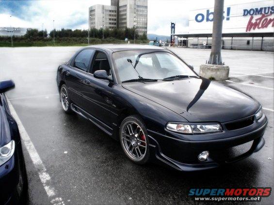 Black sedan parked in a wet parking lot, front 3/4 view. Red brake calipers visible