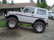 1989 Ford Bronco - A silver SUV is parked on a dirt mound with a "For Sale" sign visible in the rear window.