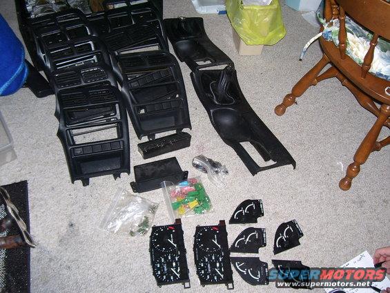 Car dashboard and center console parts, plus several gauges, laid out on a carpeted floor
