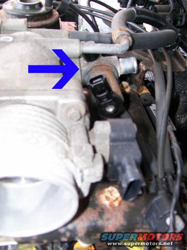 Engine part with blue arrow pointing to a sensor, showing rust and wiring