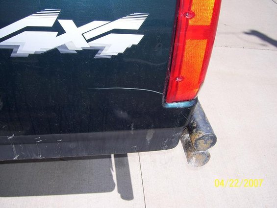 Dark green truck rear quarter panel with a white 4x4 decal and a red taillight. Dual exhaust pipes are visible below
