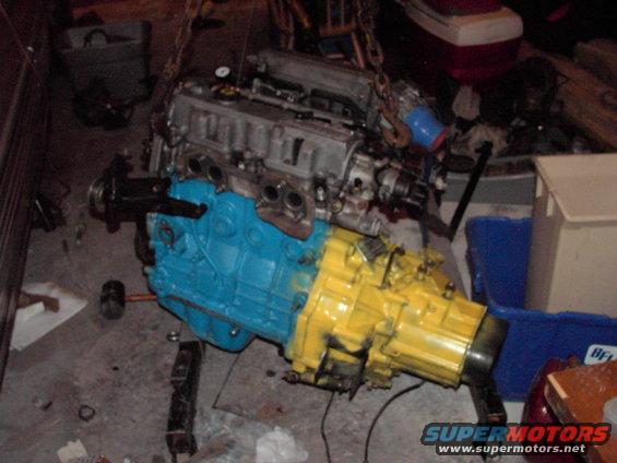 Engine and transmission assembly, painted blue and yellow, suspended by chains