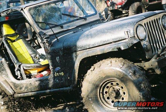 Mud-covered black Jeep CJ with yellow seats, front quarter view