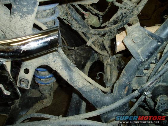 Close-up of motorcycle frame, suspension, and wiring. Shows blue springs and chrome pipe