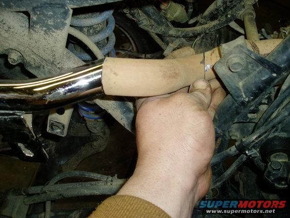 Close-up of a hand holding a chrome exhaust pipe near a tan-colored section, with suspension springs visible