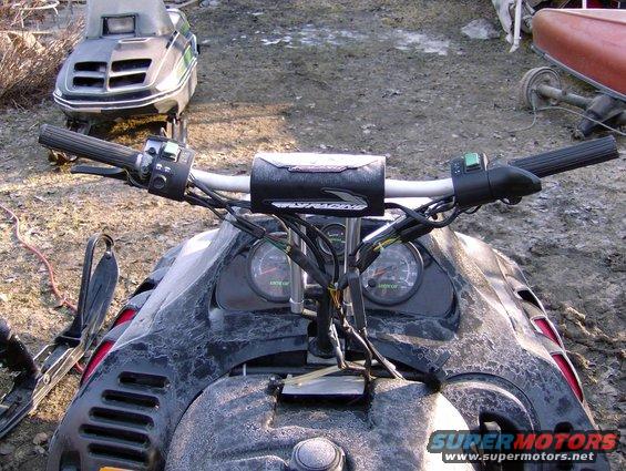 Snowmobile handlebars and gauges with another snowmobile in background