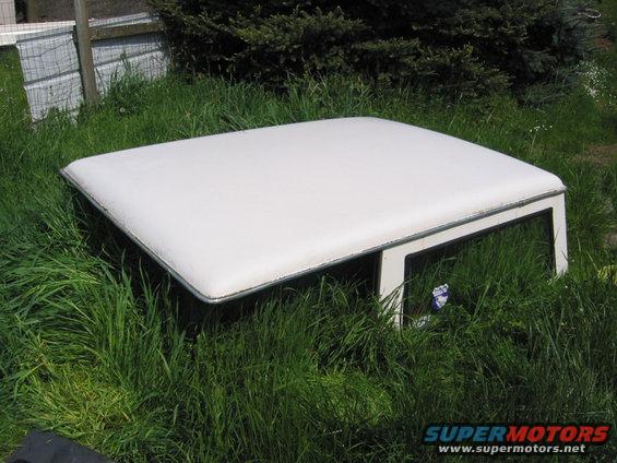 White hardtop with chrome trim, sitting in tall grass