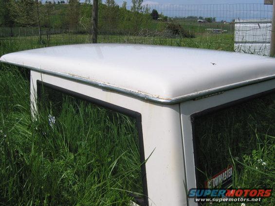 White hardtop of a vehicle overgrown with grass. Supermotors.net logo visible