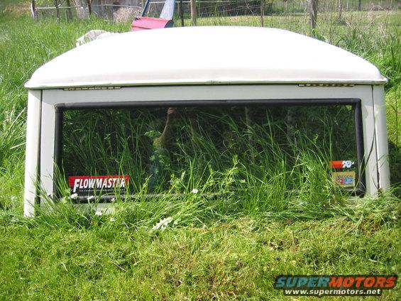 White Ford Bronco hardtop sitting in tall grass. Has a Flowmaster sticker on the rear window