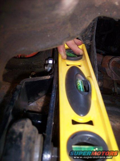 Yellow level tool against rusty vehicle undercarriage with bolts and suspension components