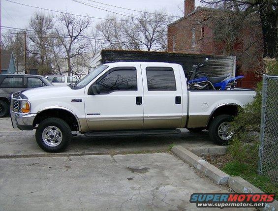 White and tan 2000 Ford F-250 crew cab pickup truck side view with a dirt bike in the bed