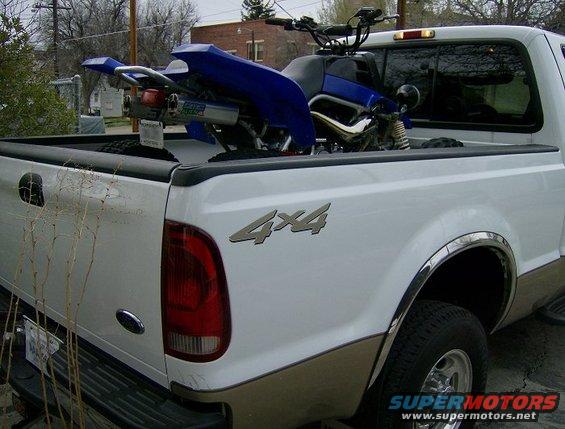White pickup truck with a blue ATV in the bed. Has 4x4 badging