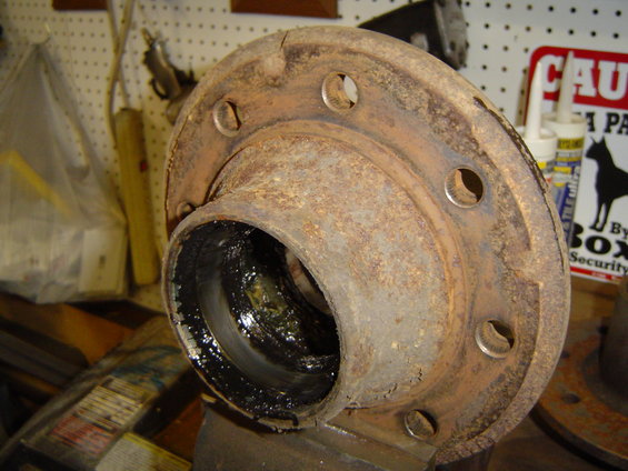 Rusted wheel hub with visible grease and bolt holes, held in a vise