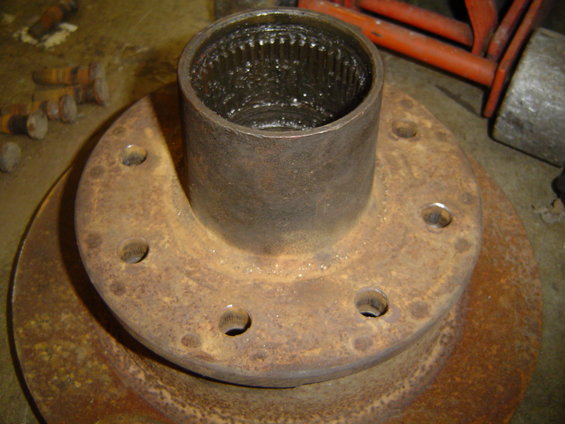 Close-up of a rusty wheel hub with splines inside, sitting on a brake rotor. Several bolts are scattered nearby