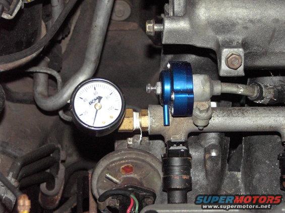 Close-up of a blue adjustable fuel pressure regulator with a DCM gauge attached to fuel lines