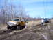 1996 Ford Bronco - Two trucks navigate a muddy off-road course under a bright blue sky.
