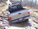 1996 Ford Bronco - A Toyota Tundra is stuck in deep mud on an incline, with a chain attached to its rear bumper.