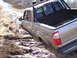 1996 Ford Bronco - A silver Toyota Tundra is stuck in thick mud on an unpaved road, with its rear passenger side wheel submerged.